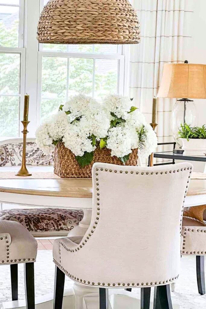 classic oval dining table and nailhead chairs with a trendy patterned bench and basket of white hydrangeas