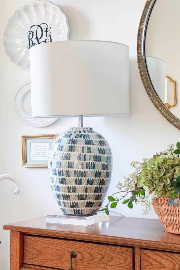 wood entry console styled with a mosaic tile lamp, monogrammed decorative plates, and a basket of green hydrangeas