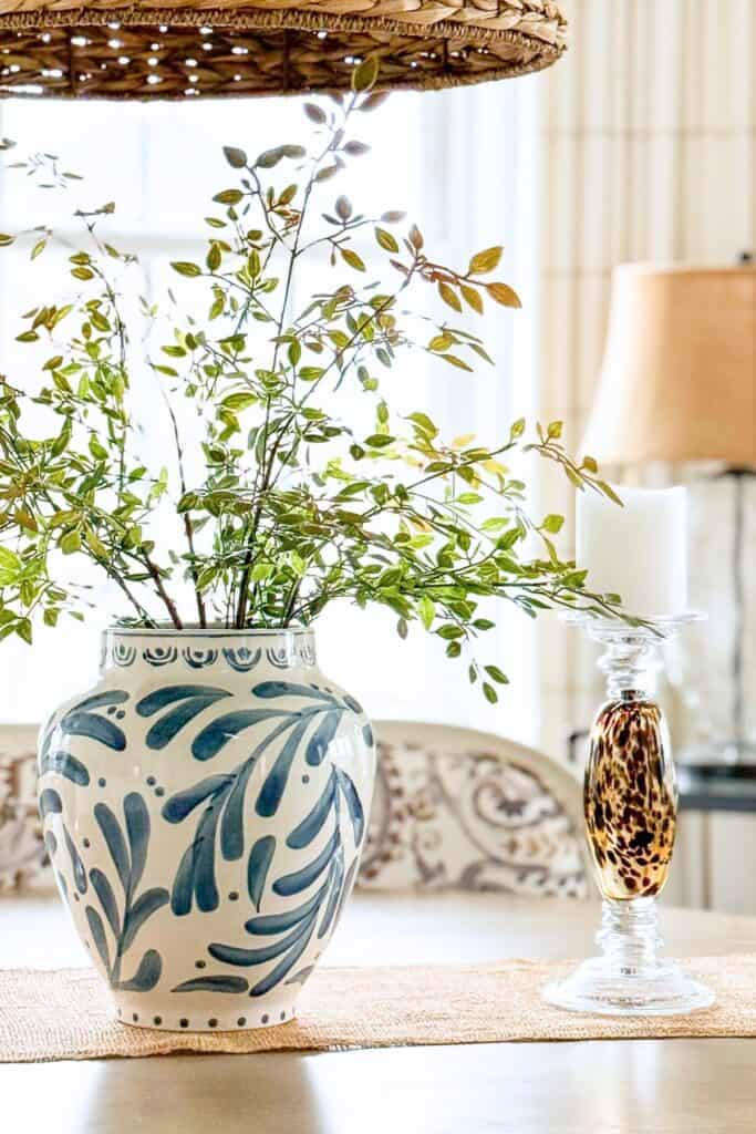 hand painted blue and cream vase with greenery next to a tortoiseshell glass candlestick on a dining table