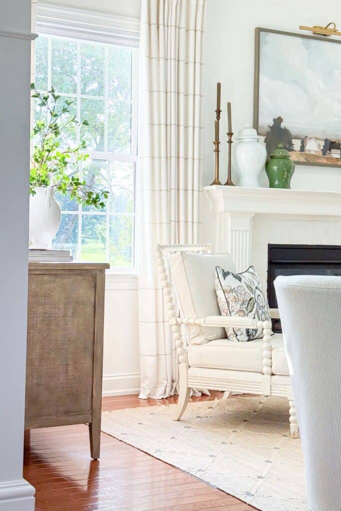 white fireplace mantel styled with brass candlesticks and ginger jars, next to a classic spindle chair with a floral pillow