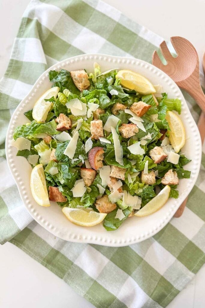 CAESAR SALAD IN A WHITE BOWL WITH WOODEN SERVERS