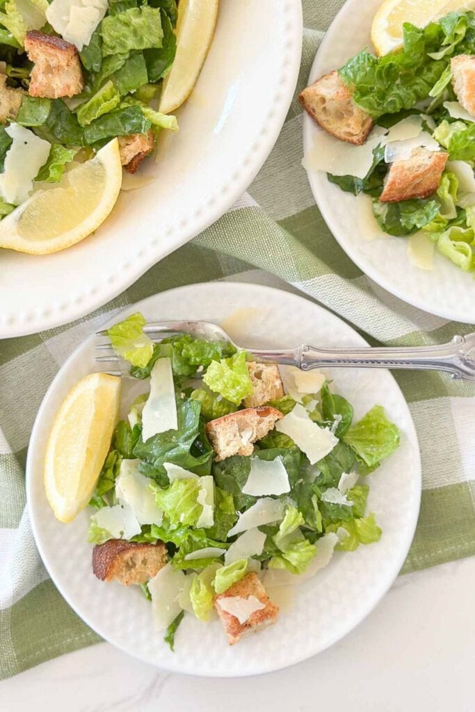 Caesar salad on white plates with lemon slices
