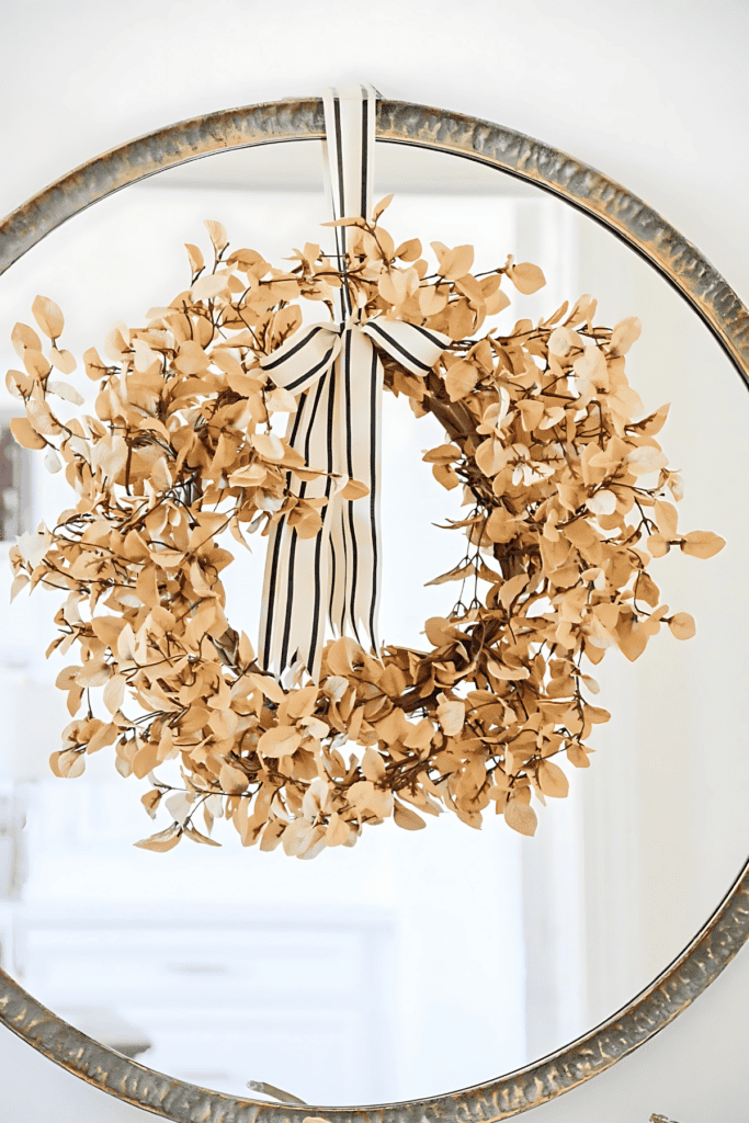 round mirror with faded camel colored leaves tied with a black and cream colored bow.