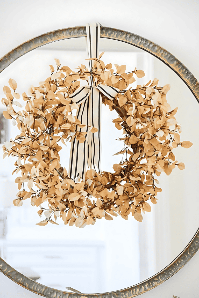 dried leaf wreath hanging on a round mirror with a black and white bow