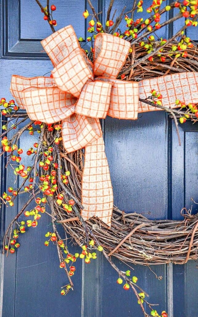 fall grapevine wreath with bittersweet berries and an orange plaid ribbon bow on a navy front door
