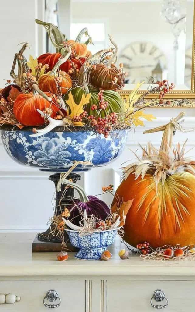 orange, green, and purple velvet pumpkins in a blue and white bowl with a faux pumpkin beside it