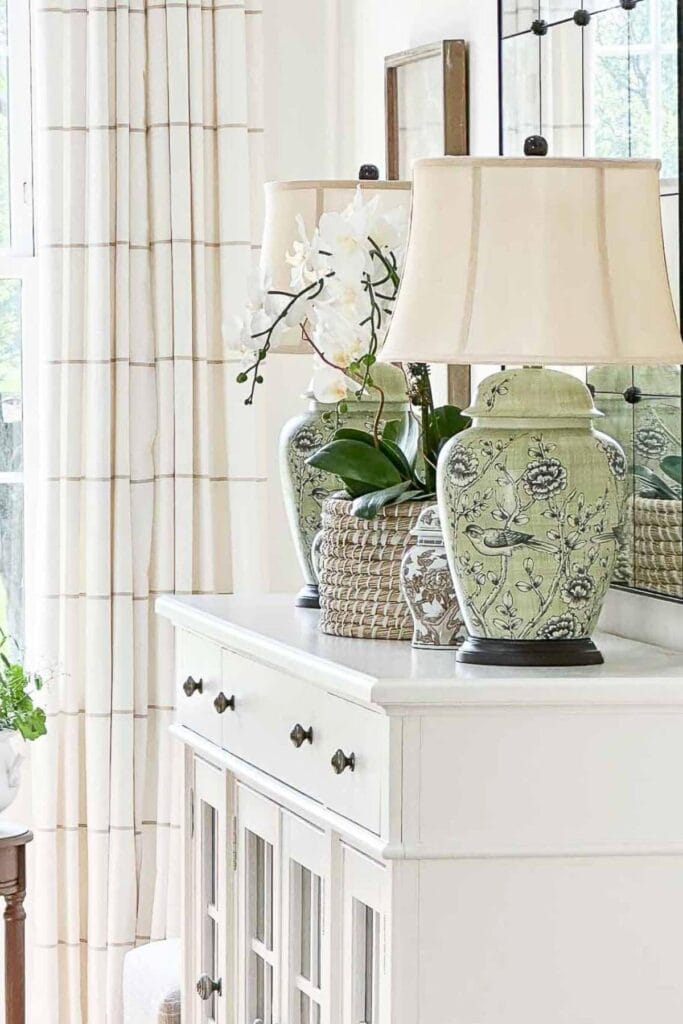 white buffet styled with green ginger jar lamps and neutral decor showing how to decorate with color in a cohesive palette