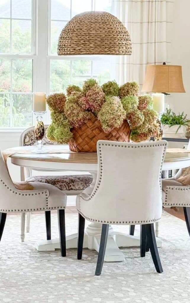 dried green and pink hydrangeas in a woven basket centerpiece on a round dining table with nailhead chairs