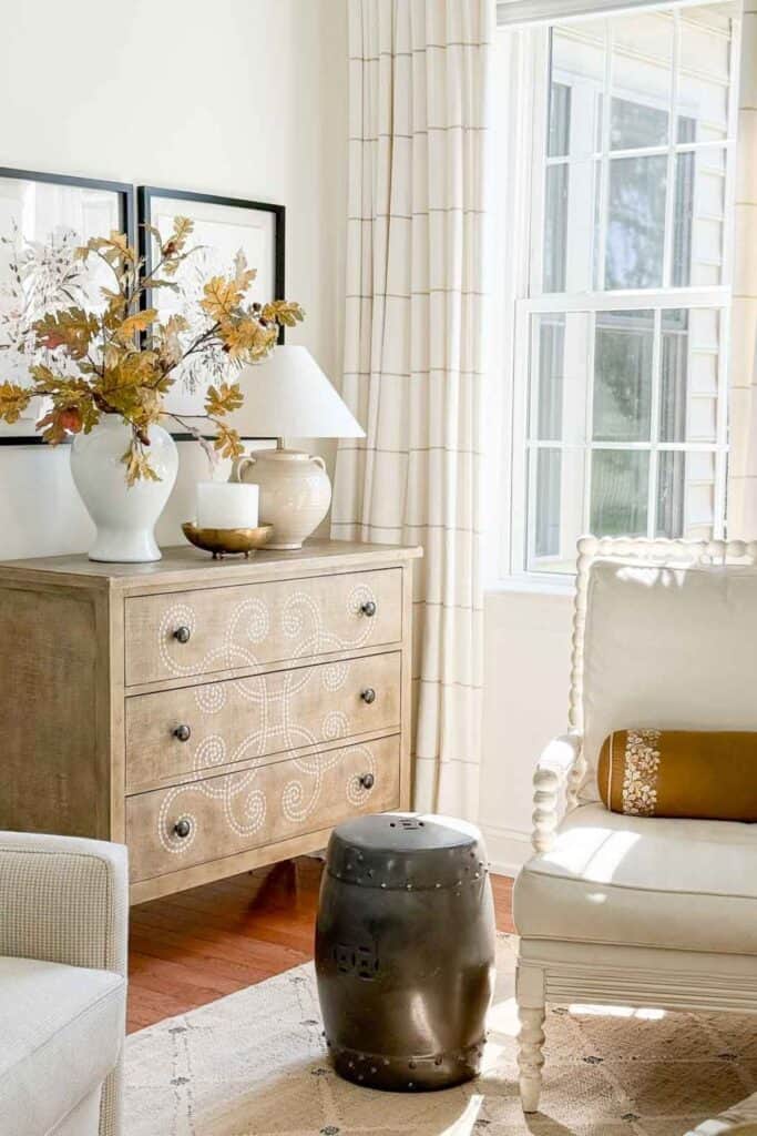 fall oak leaf branches in a white vase on a wood dresser in a neutral living room