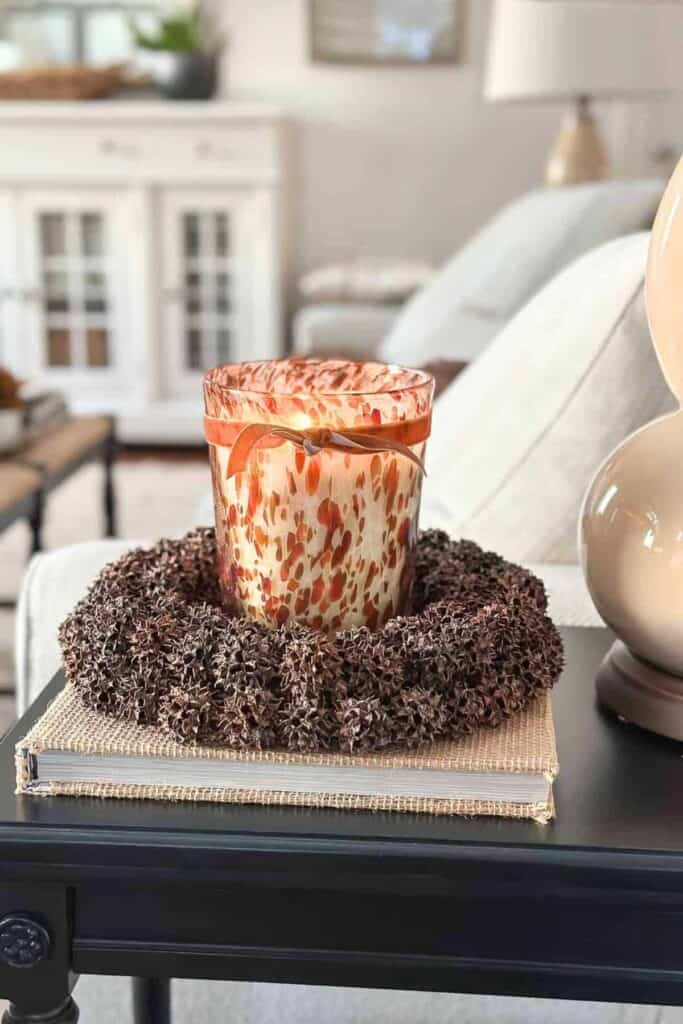 a beautiful orange speckled candle holder with a fall scented candle inside. It sits in a spikey gum ball