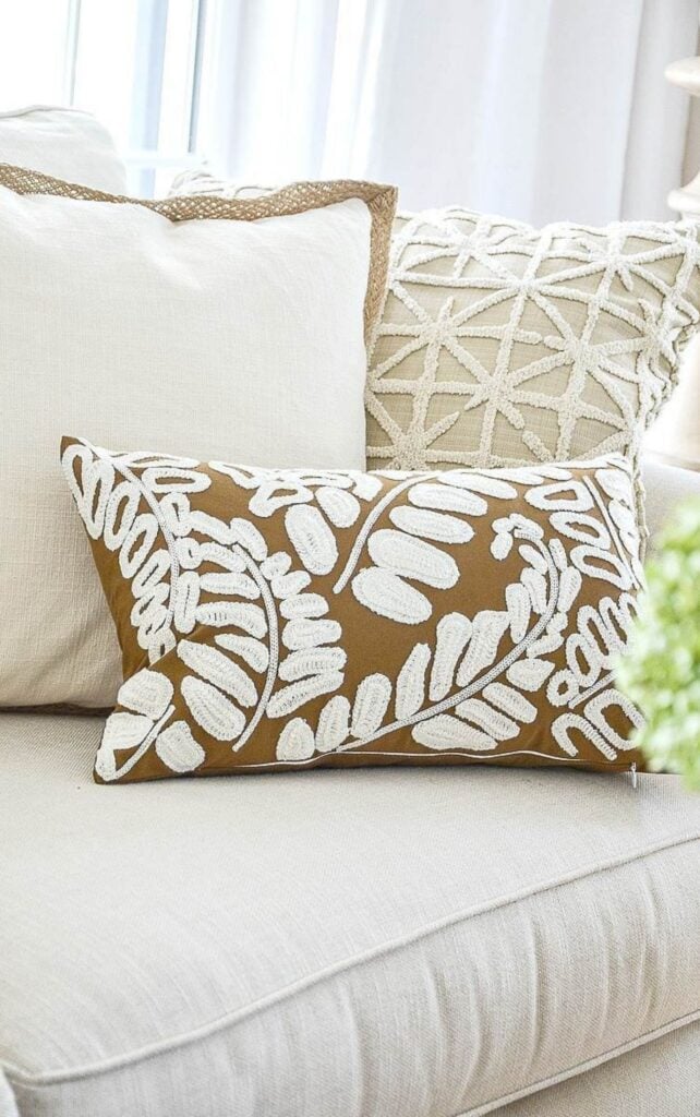 cream, jute trimmed, and fern embroidered fall throw pillows layered on a neutral sofa