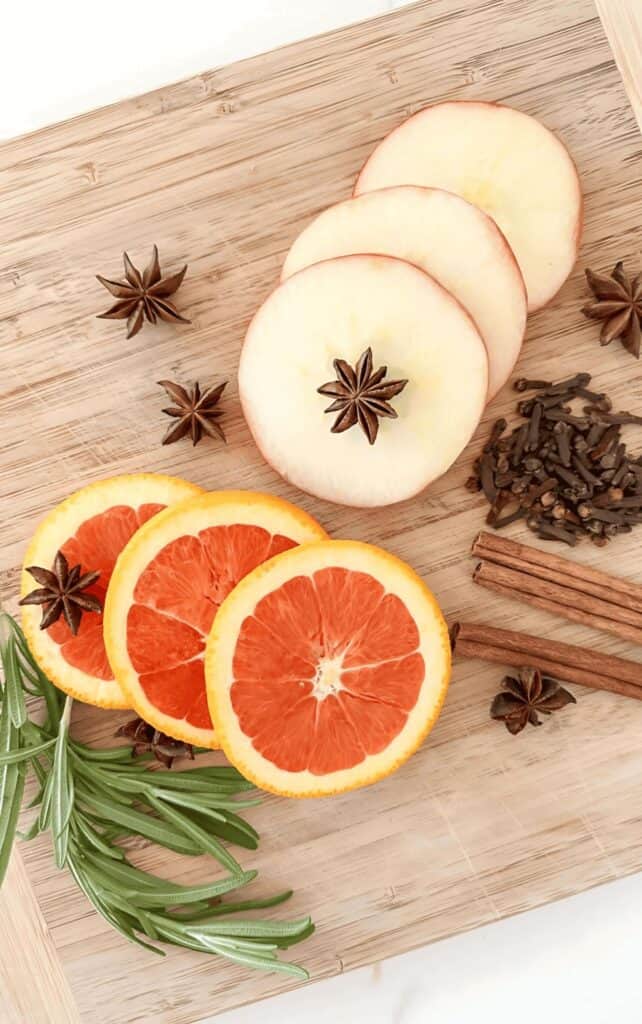 fall simmer pot ingredients including sliced apples, orange, cinnamon sticks, cloves, star anise, and rosemary on a wood cutting board