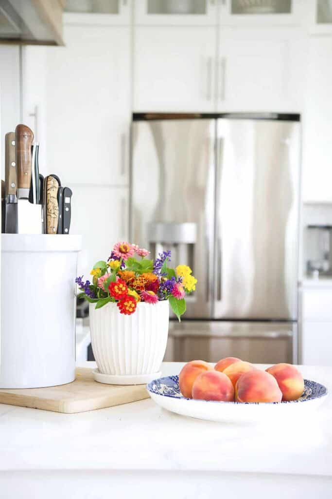 summer cut flowers and a bowl of peaches near a work station in the kitchen