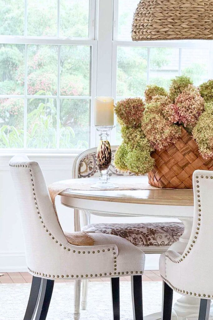woven basket of pink and green dried hydrangeas on a dining table with upholstered chairs