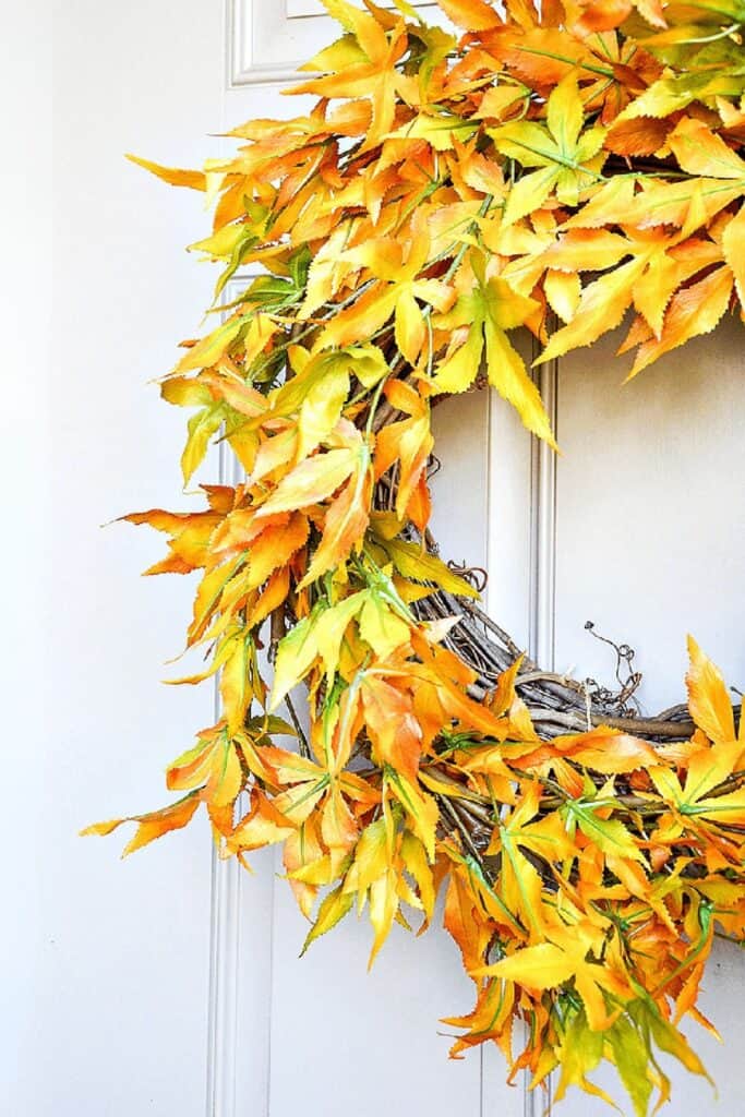 Close up of a fall leaf wreath in orange, yellow, and green hanging on a white front door