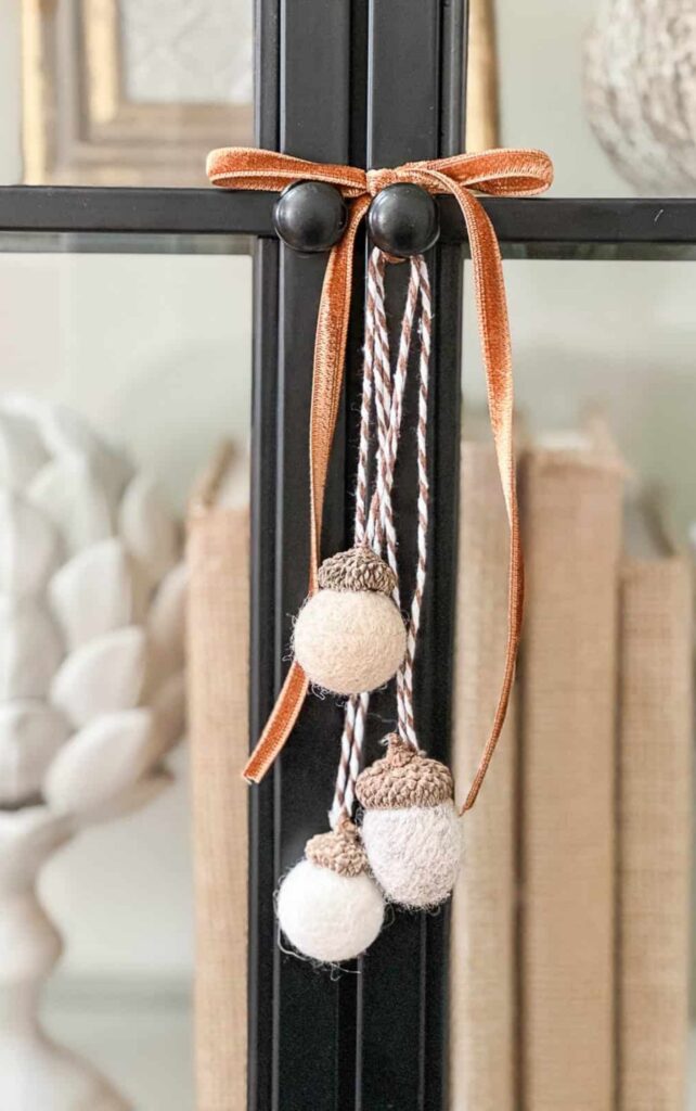 Felted wool ball acorns tied with velvet ribbon hanging from a black framed mirror