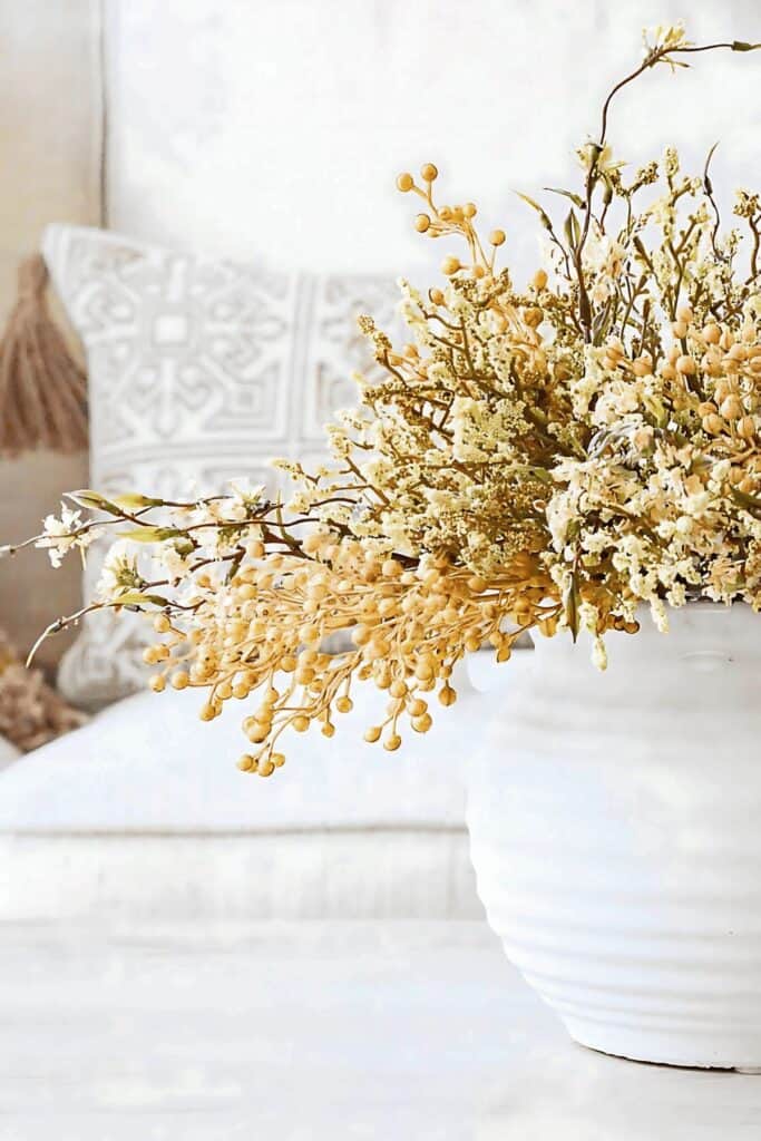 Dried yellow fall floral arrangement in a white ribbed vase with a neutral patterned pillow in the background