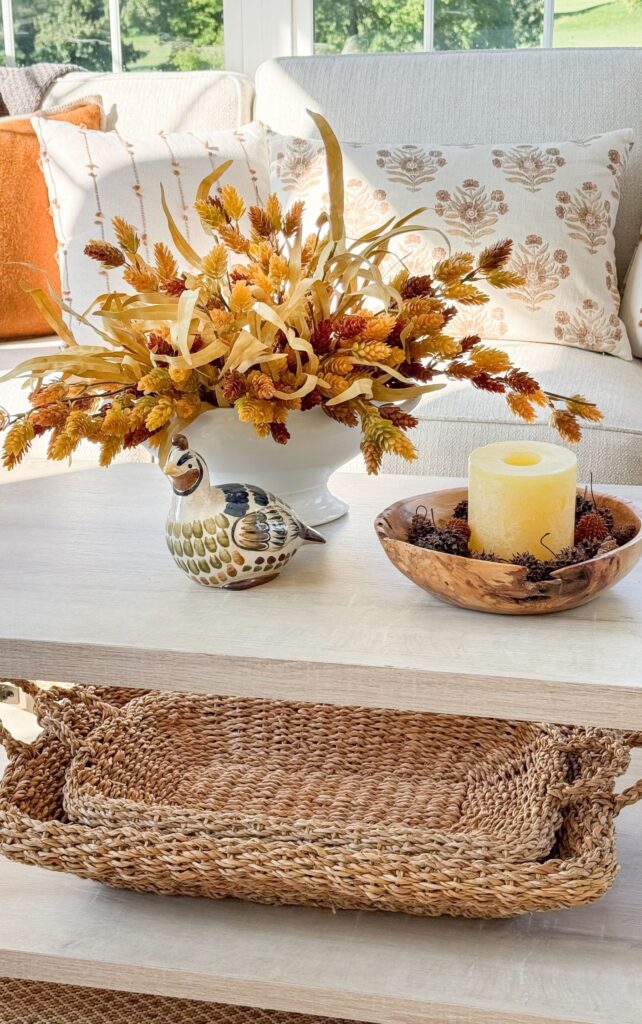 Dried grasses and seed pods arrangement in a white urn on a coffee table with pinecones and a candle
