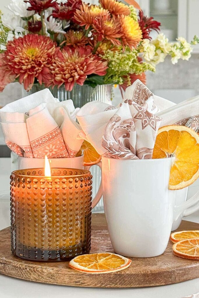 A lit hobnail glass candle beside a dried orange slice on a coffee bar styled for fall.