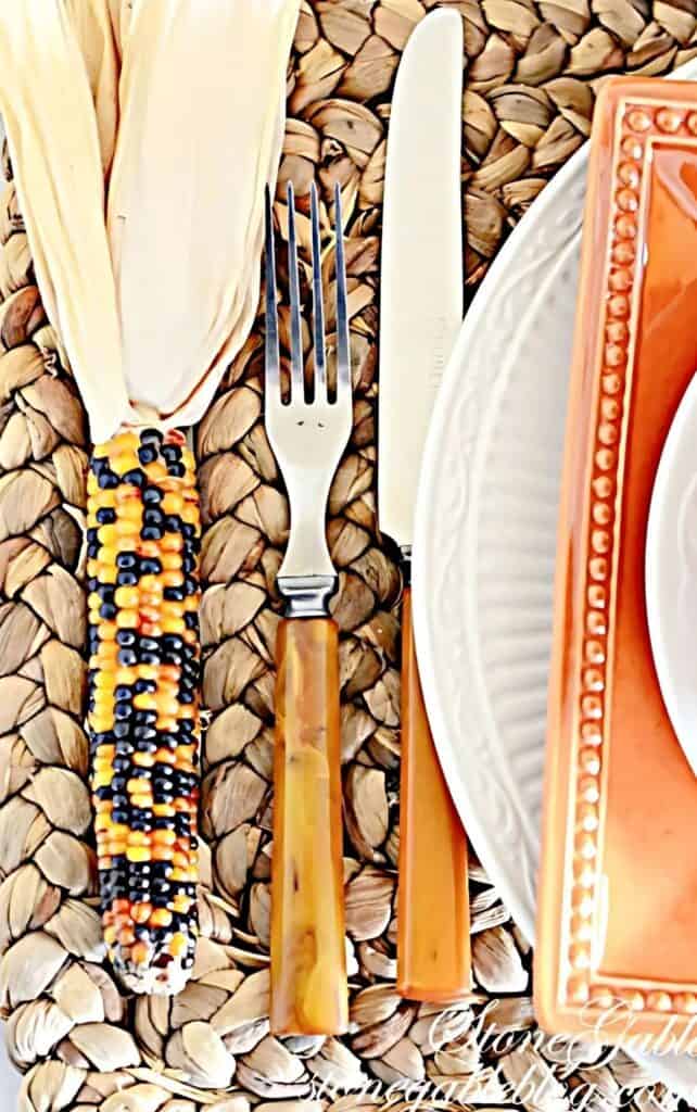 An ear of Indian corn beside a fork, knife, and plate at a Thanksgiving place setting