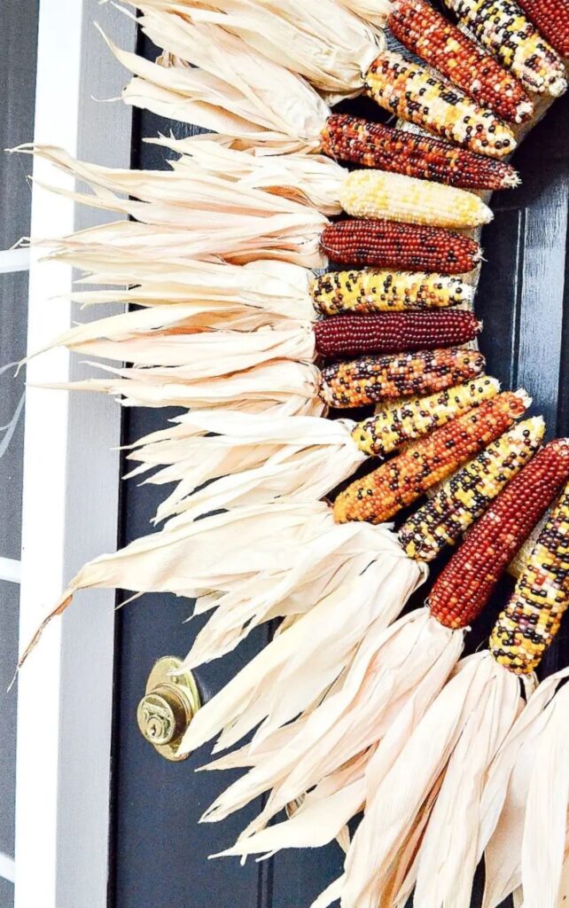 Indian corn wreath with husks in shades of red, yellow, and purple on a black door