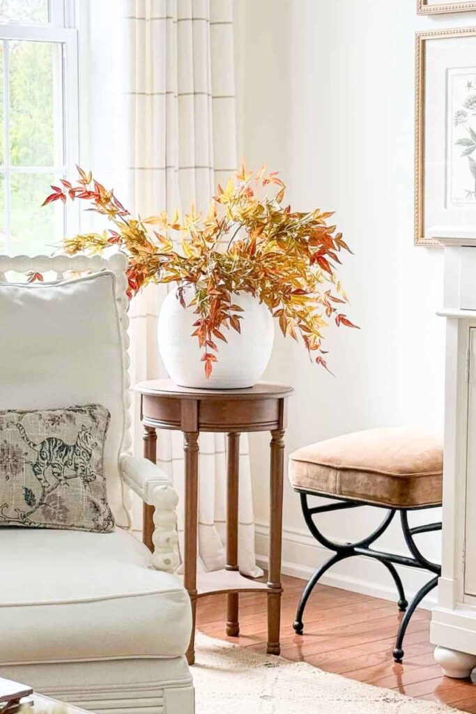 Faux orange fall stems in a textured white round vase on a wood side table, styled for budget friendly fall decorating.