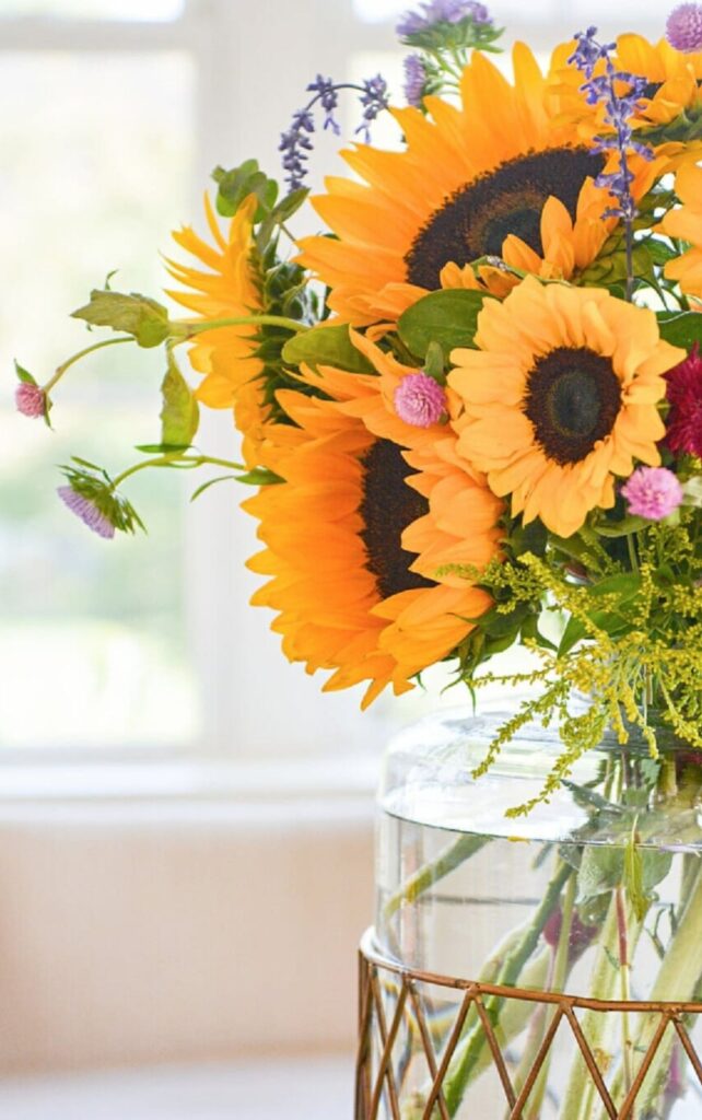 Sunflowers with purple and pink wildflowers in a glass vase by a window