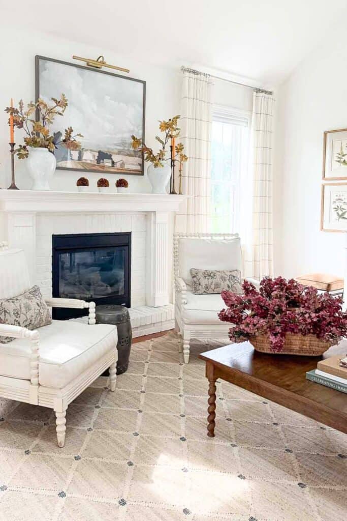 Living room with white mantel styled for fall with vases of leaves and candles, dried hydrangeas in a basket on the coffee table