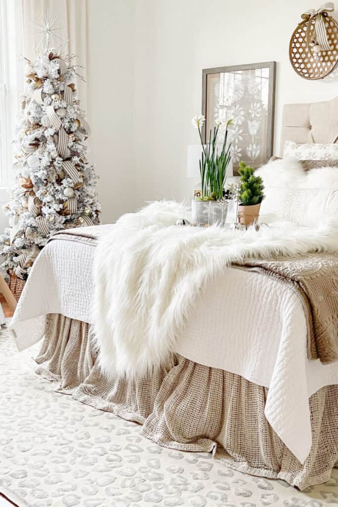Neutral Christmas bedroom with white faux fur throw, small Christmas tree, and cozy layered bedding