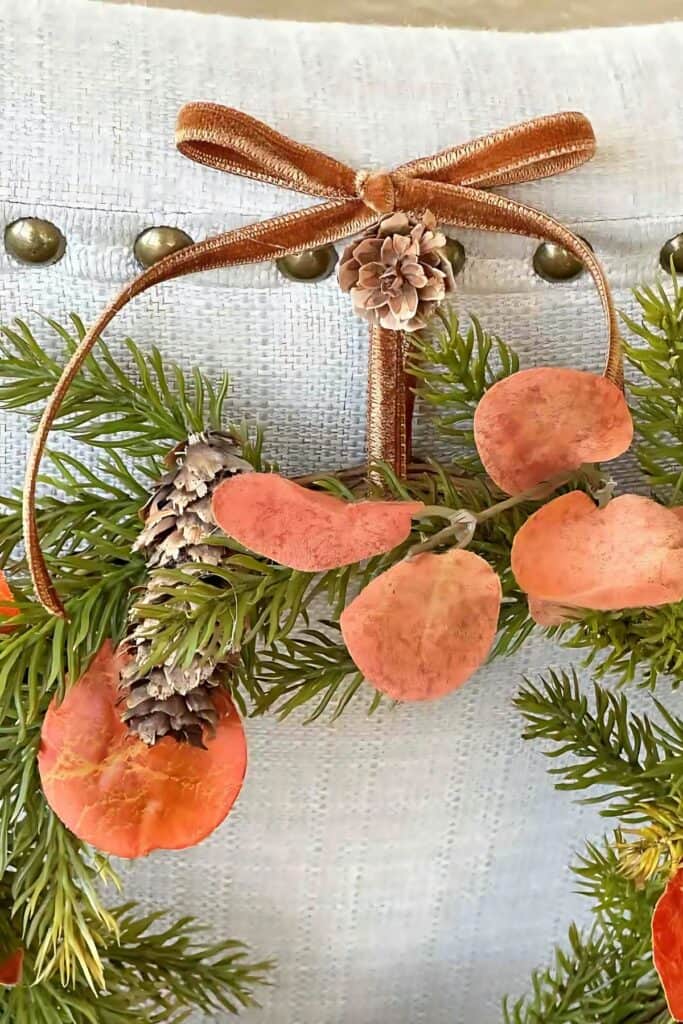 Copper velvet bow with pinecones, greenery, and orange leaves on a Christmas wreath 