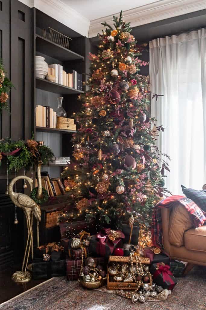 A traditional Christmas tree decorated with deep burgundy, red, and green ornaments accented by gold details, showing the 2025 updated red and green Christmas trend.