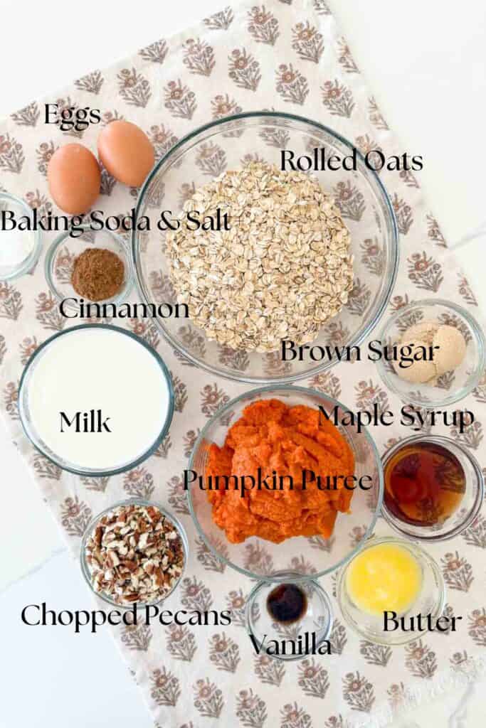 Overhead view of labeled ingredients for Pumpkin Baked Oatmeal including oats, pumpkin puree, brown sugar, milk, eggs, and spices in glass bowls.