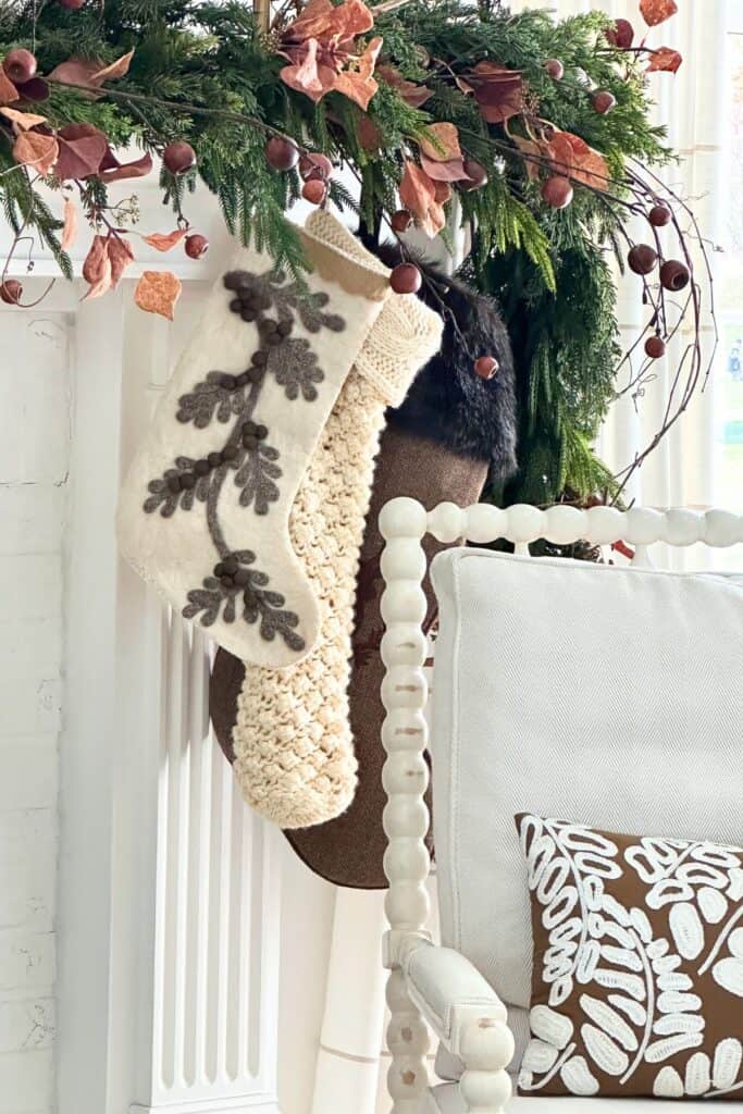 A Christmas mantel decorated with rust-colored leaves, pine greenery, and cozy knit stockings — showing the warm autumn-inspired Christmas trend for 2025.