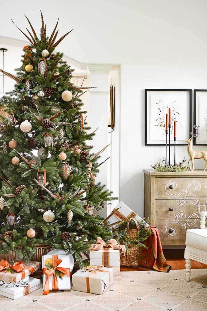 A Christmas tree decorated with pheasant feathers, pinecones, and neutral ornaments, surrounded by wrapped gifts in warm copper and gold ribbons — showcasing the 2025 autumn-inspired Christmas color trend.