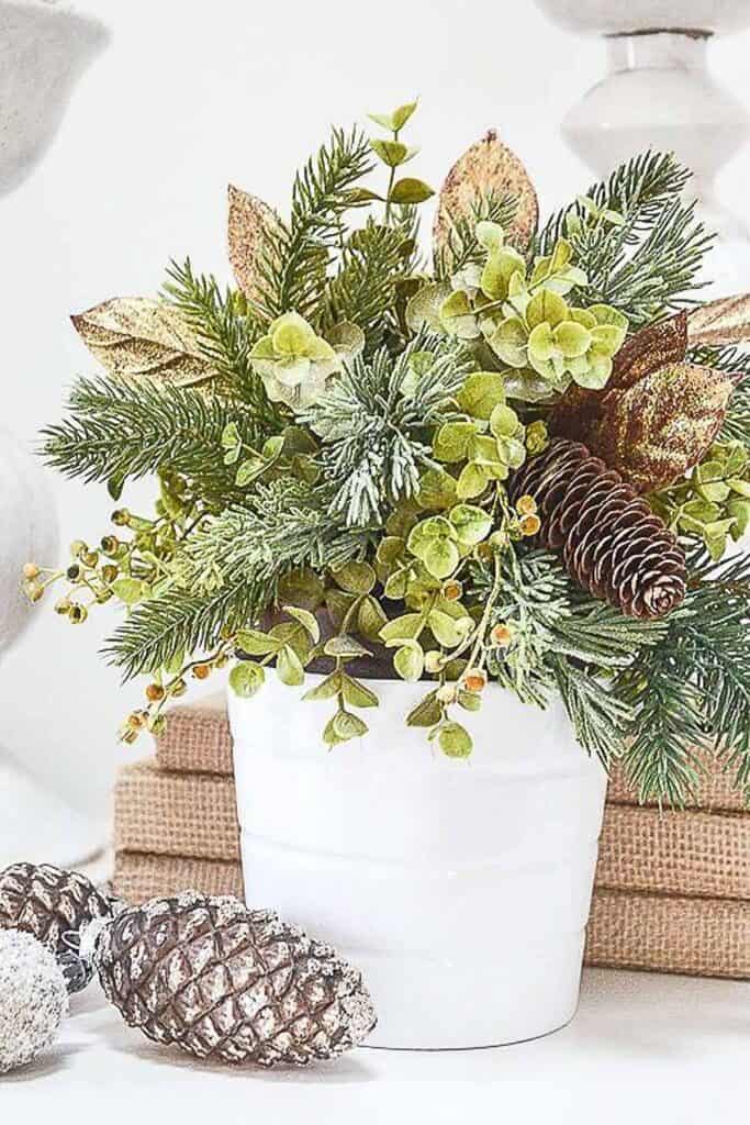 Christmas 2025 decorating trend featuring a mix of greenery, pinecones, and metallic leaves arranged in a white pot for a fresh holiday look.
