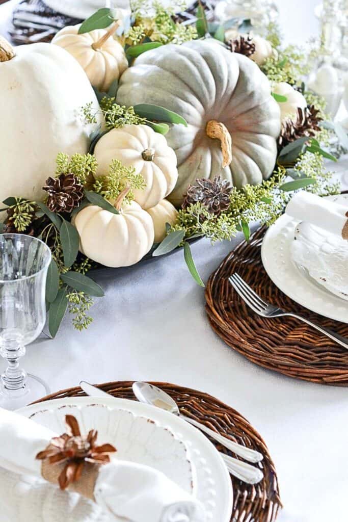 Elegant fall table decorated with white and green pumpkins, pinecones, and eucalyptus for a natural seasonal centerpiece.