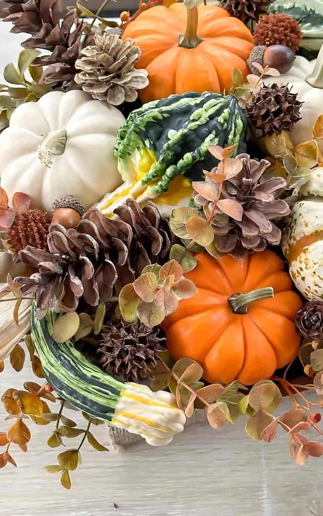 Fall arrangement of orange and white mini pumpkins, green gourds, pinecones, sweetgum pods, acorns, and autumn eucalyptus leaves, a budget friendly idea for decorating with pumpkins.