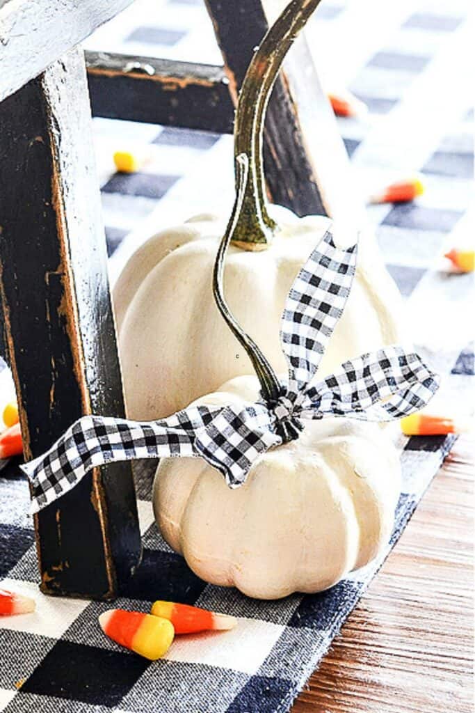 White faux pumpkins with real stems styled with black-and-white gingham ribbon on a buffalo check cloth for fall decorating without orange.