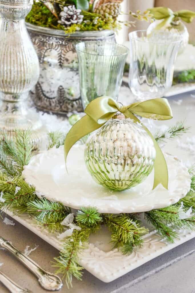 Elegant Christmas table setting with green ornament, greenery wreath, and white plate showing the green Christmas decor trend for 2025.
