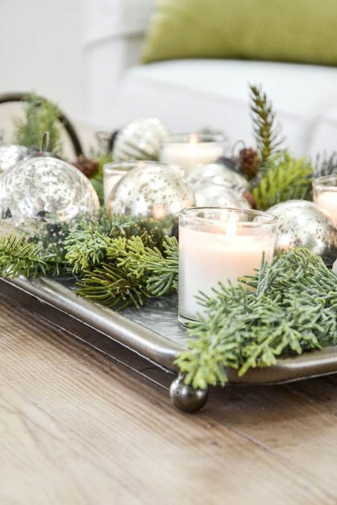 Christmas candle centerpiece with evergreens and mercury glass ornaments on a silver tray showing the green Christmas decor trend for 2025.