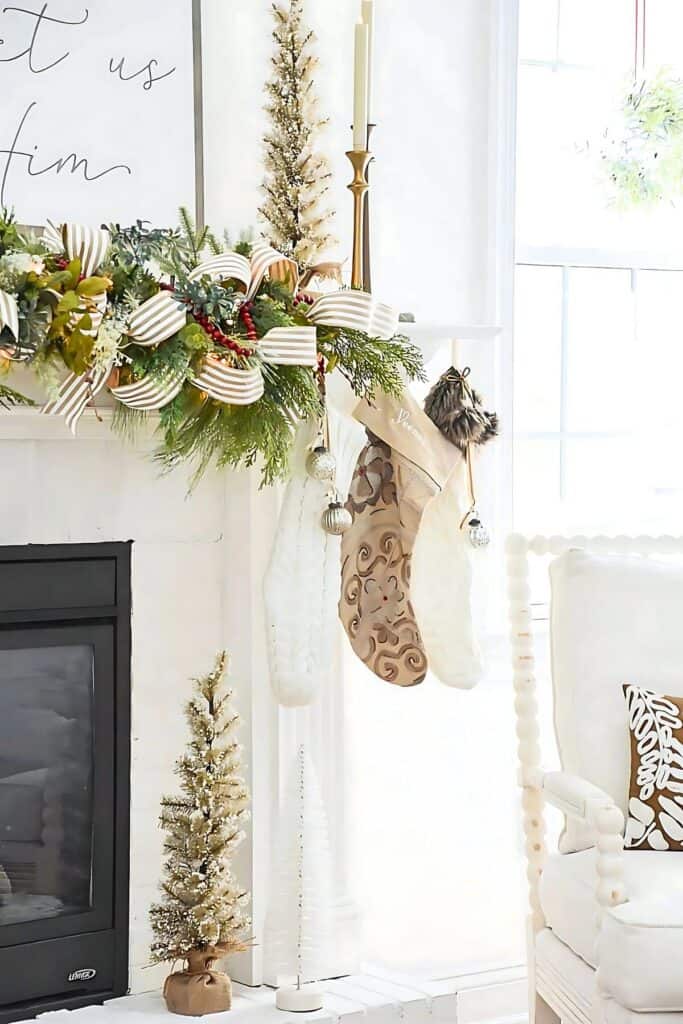 Elegant neutral Christmas mantel with greenery, striped ribbon, and white knit stockings showcasing the green and neutral Christmas decor trend for 2025.