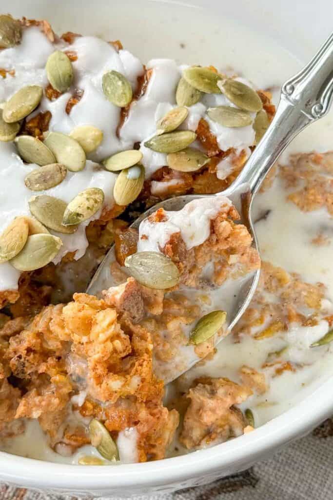 Spoonful of Pumpkin Baked Oatmeal with glaze and pumpkin seeds lifted above a bowl of warm oatmeal