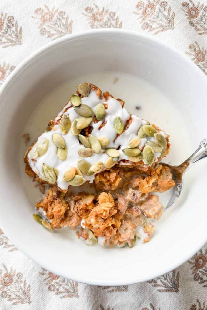 Warm Pumpkin Baked Oatmeal served in a white bowl with milk, topped with pumpkin seeds and glaze.