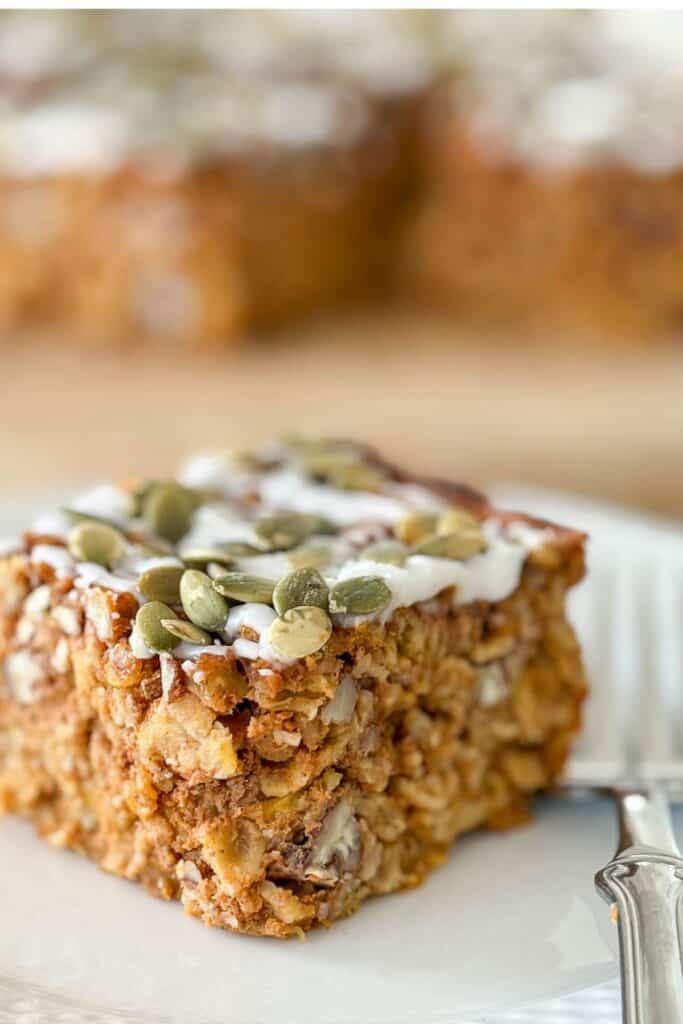 Close-up of a slice of Pumpkin Baked Oatmeal topped with vanilla drizzle and pumpkin seeds on a white plate.