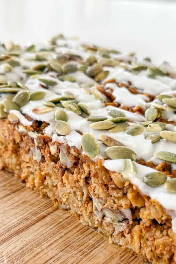 Pumpkin Baked Oatmeal in a square pan topped with vanilla drizzle and pumpkin seeds on a wooden board
