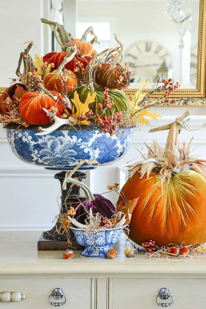Velvet pumpkins in blue and white chinoiserie bowls with autumn leaves and berries, elegant fall centerpiece idea for dining room or buffet.