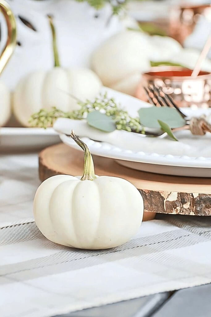 White pumpkin on a fall table with eucalyptus, white dishes, and copper accents for an elegant autumn tablescape.