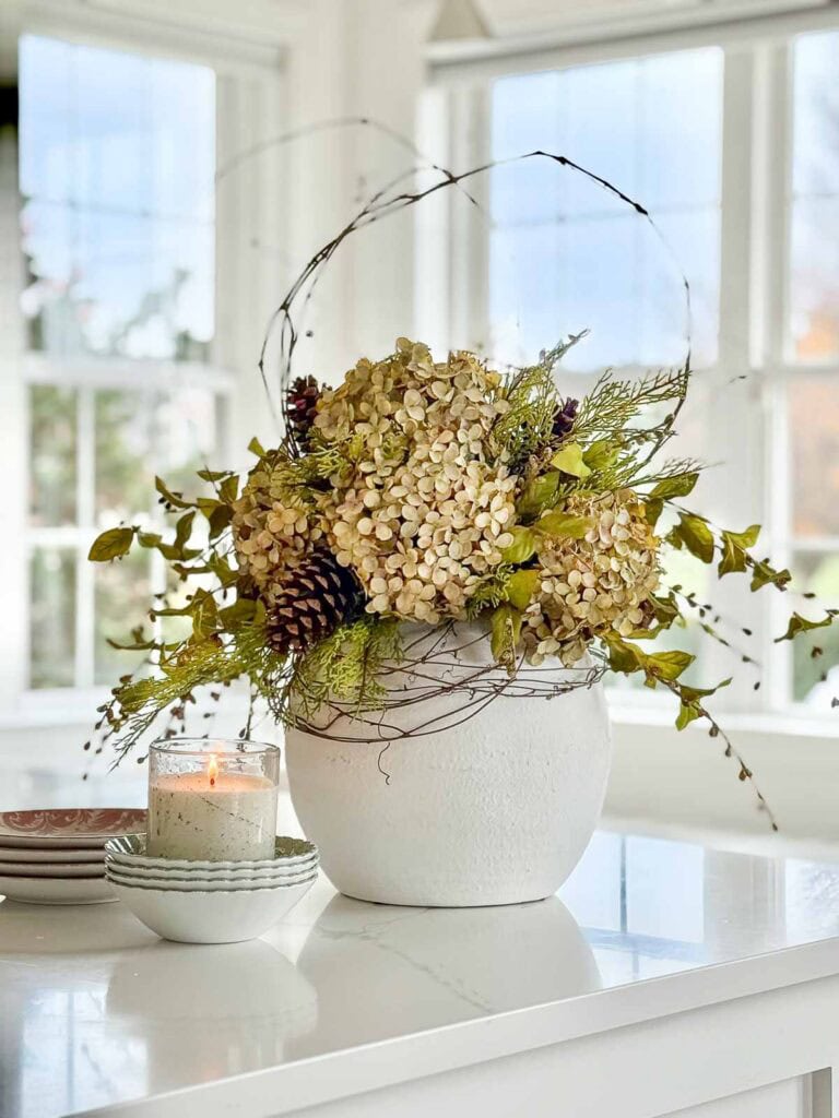 arrangement of dried hydrangeas mixed with faux Christmas greens in a white pot on a kitchen island