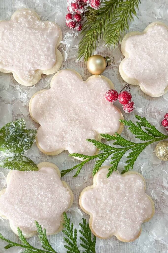 Iced cut out sugar cookies with a soft pink glaze and sanding sugar, styled with Christmas greens and berries