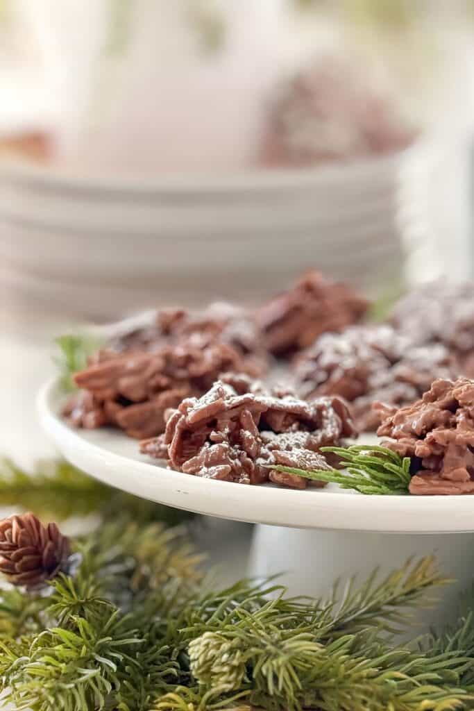 No bake haystack cookies on a white cake stand with powdered sugar and Christmas greenery